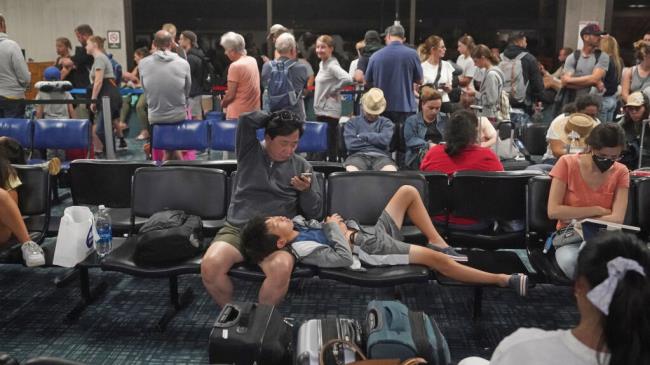 People gather at the Kahului Airport while waiting for flights Wednesday, Aug. 9, 2023, in Kahului, Hawaii. Several thousand Hawaii residents raced to escape homes on Maui as the Lahaina fire swept across the island, killing multiple people and burning parts of a centuries-old town. (AP Photo/Rick Bowmer)