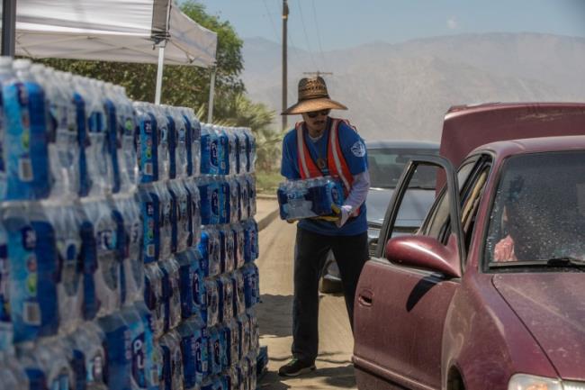 A member of TODEC loads a crate of bottled water into a resident's vehicle outside Oasis Mobile Home Park in Coachella Valley on Aug. 24, 2023.